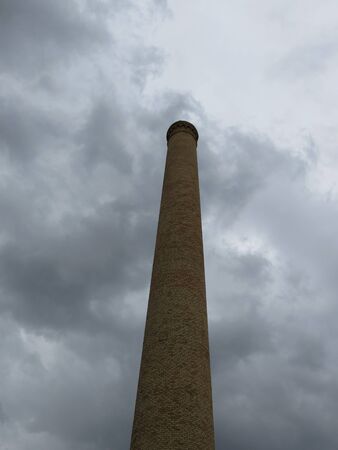 Tall brick chimney against cloudy sky useful as industrial or pollution conceptの写真素材