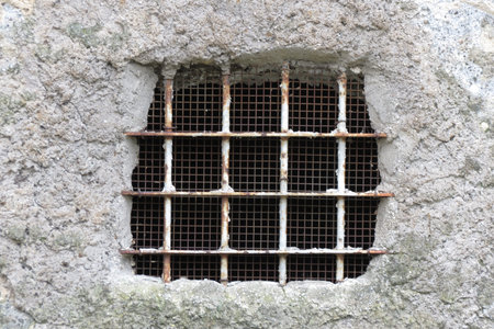 Old window opening in a stone wall with iron gratening