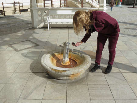 KARLOVY VARY, CZECH REPUBLIC - CIRCA MARCH 2019: unidentified girl fetching thermal water from a public fountainのeditorial素材