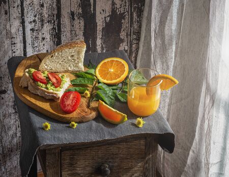 Healthy vegetarian breakfast with bread, avocados, tomatoes and orange juice, prepared at home during the quarantine.の写真素材