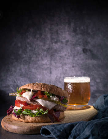 One homemade hamburger with arugula, tomato and cheese and drinks on a dark backgroundの写真素材