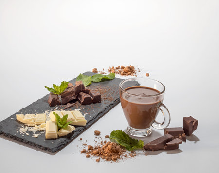 Chunks of dark and white chocolate presented on a slate board with mint leaves. Cup of chocolate on...