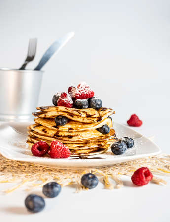 Stack of pancakes with forest fruit, raspberry, blueberry, chocolate scirope and icing sugar on a light-colored plate. White background.の写真素材