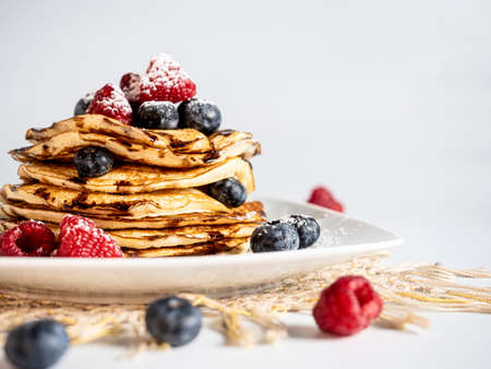 Stack of pancakes with forest fruit, raspberry, blueberry, chocolate scirope and icing sugar on a light-colored plate. White background.の写真素材