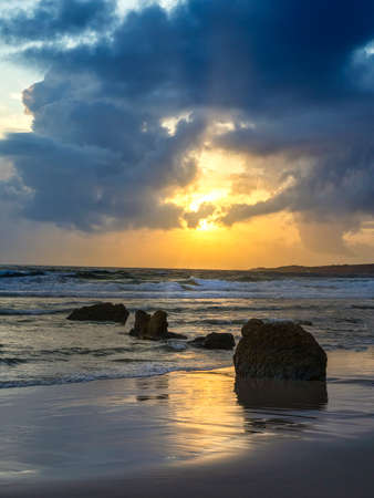 Beautiful sunset on the beach of Bologna, coast of Cadiz, Spain. Cloudy sky, orange and blue colors, orange reflections on the waves of the sea.の写真素材