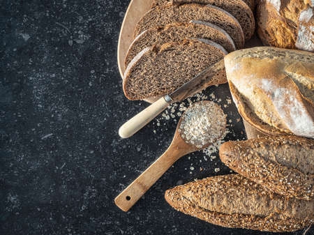 Fresh buns, whole wheat bread, sourdough and bread cut with a rolling pin and flour. On black background of rustic granite. Space for copying.の写真素材