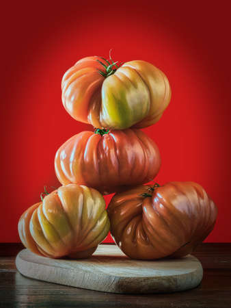 Close-up of four ripe tomatoes placed on a wooden board, forming a pyramidal figure. Red background. Beefsteak tomatoes.の写真素材