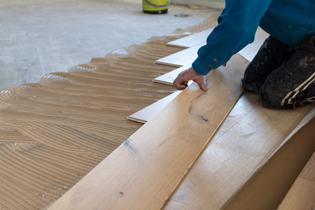 Renovation of an apartment, skilled worker uses a plastic hammer when installing pre-finished interlocking parquet. Laying with brown glue on an existing floor. Installation of oak colored parquetの写真素材