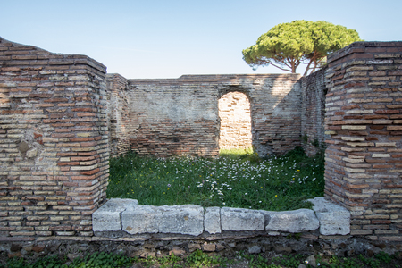 ancient Roman villa in ancient Ostia, perimeter walls in bricks and central area with green grass and spring flowers, door of the villa in the background. sea pine in the backgroundの写真素材