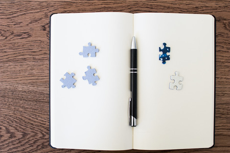 A white notebook on a wooden table with two puzzle pieces and a pen in the middle, one of the tiles with the face down and one up. Concept for opposing ideas and find a solution to complex problems.の写真素材