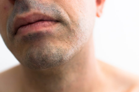 mouth of a man with a shaved beard. detail of the lips in the foreground with blurred white...