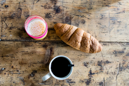 white cup of black coffee with teaspoon on a rough wooden table with veins. Breakfast with orange coffee and brioches on a wooden work tableの写真素材