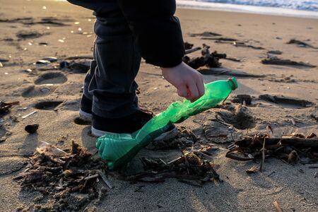 Child collect plastic bottle on ocean sea shore,sunset horizon and waves motionの写真素材