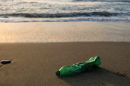 Green Plastic bottle on sea coast,sunset golden light,polluted ecosystem concept