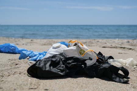 Ffp protective virus mask and plastic gloves garbage trash on sandy sea coast,coronavirus covid...