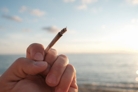 Human hand hold a tobacco cigarette over on sunset sea background,smoking addiction issue