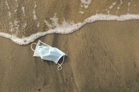 Medical face mask discarded on sea tar polluted shore,covid19 disease pollutionの写真素材