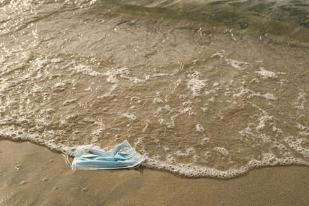 Discarded surgical face mask floating on dirty sea shore,covid19 pandemic pollutionの写真素材