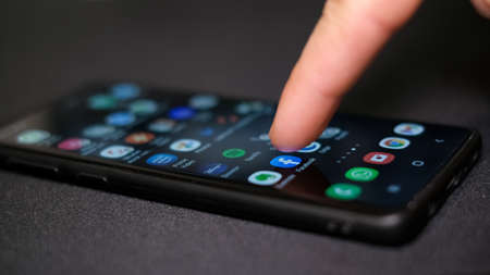 Man hand close up while tapping on Facebook app icon on a smartphone,social network tech addictionのeditorial素材