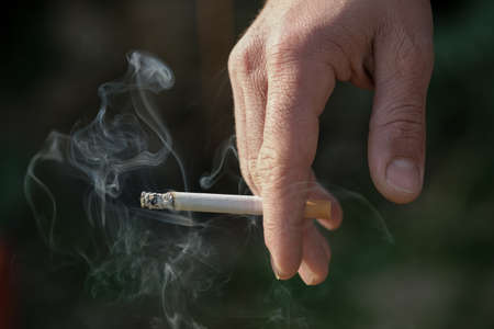 Man hand hold burning cigarette while smoking,tobacco smoke addiction,unhealthy lifestyleの写真素材