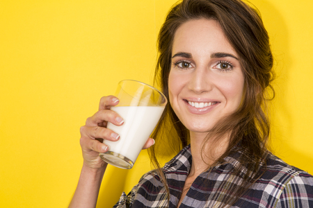 young woman drink milk on yellow backgroundの写真素材