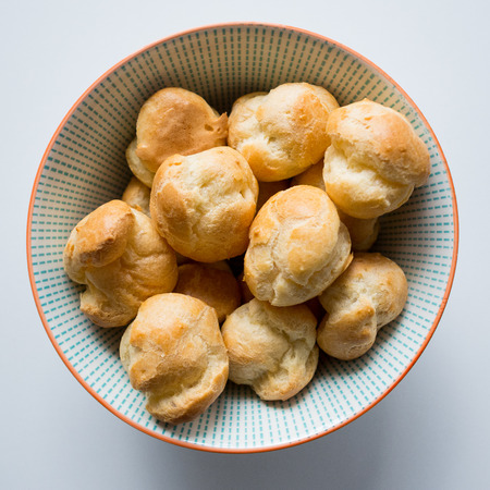 Top view of cream puffs in a blue dotted bowl on a white table. Squared format.の写真素材
