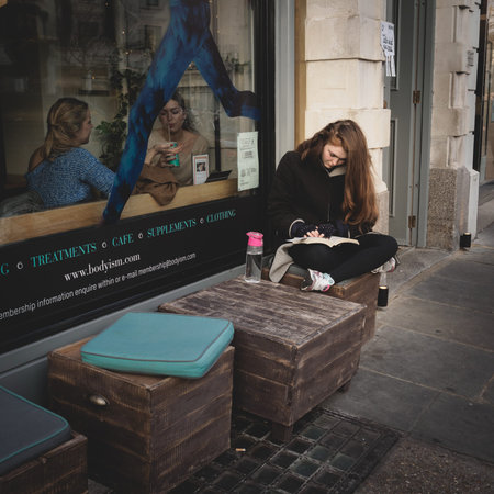 Girl reading a book outside a cafÃƒÂ© in Notting Hill. London (UK). March 2017. Squared format.