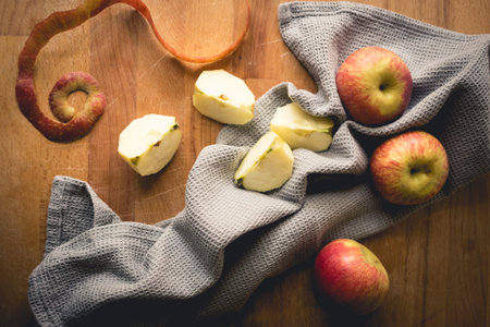 Top view of apples on a wooden chopping board with a grey kitchen cloth. Landscape format.