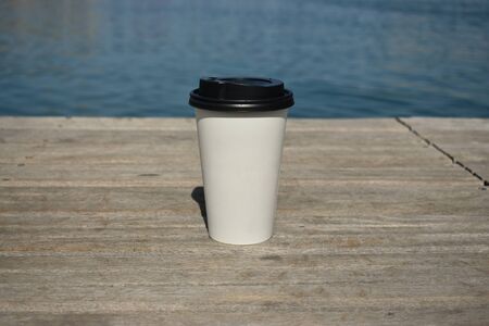 Paper cup of coffee on the background of the sea on the boardsの写真素材