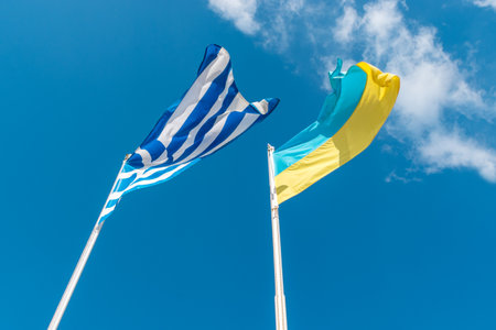 Ukrainian flag with Greek flag on background of blue skyの写真素材