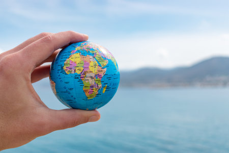 Human hand is holding small globe in front of blue sky. Global issues conceptの写真素材