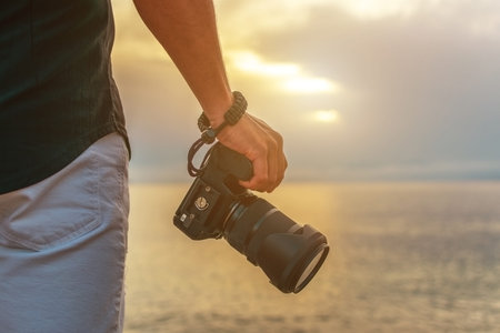 Man holds a camera in his hand at sunset.
