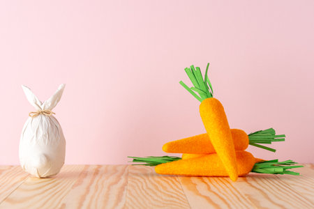 Easter egg wrapped in a paper in the shape of a bunny with carrots. Minimal Easter background. Spring holidays concept.の写真素材