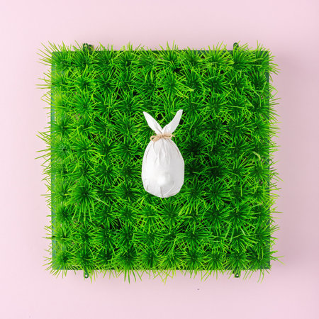 Creative composition with egg wrapped in a paper in the shape of a bunny on green grass. Easter...