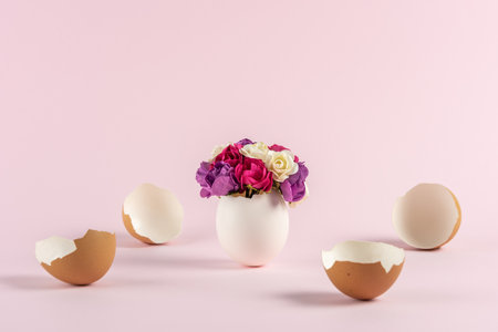 Spring flowers in cracked eggshell with broken Easter eggs against pastel pink background. Easter minimal concept. Creative Happy Easter or spring layout.の写真素材