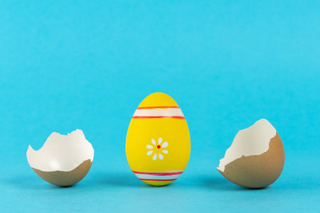 Empty eggshell with color Easter egg on pastel blue background. Minimal Easter holiday concept.