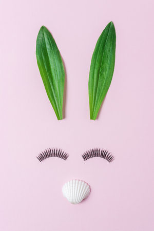 Bunny face made of natural green leaves with eyelashes on pastel pink background. Easter minimal concept. Flat lay.の写真素材