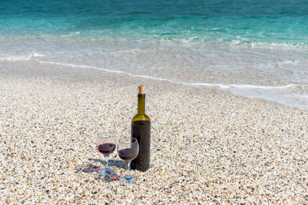 Glasses of red wine and bottle on the beach at the summer sunny day. Sea on the background.の写真素材