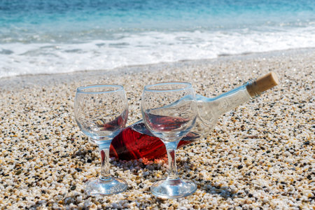 Bottle of red wine with wine glasses on the beach at the summer sunny day. Sea on the background.の写真素材