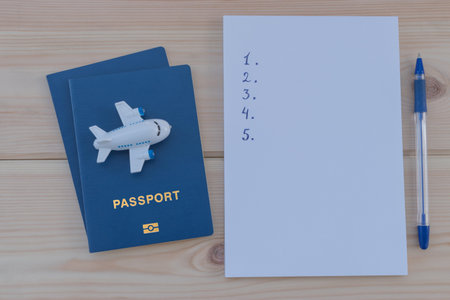 Small toy plane on top of a blue passport and white notebook on wooden table.