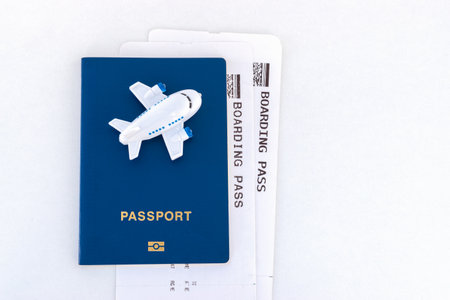 Small toy plane on top of a blue passport with boarding pass on a white background.の写真素材