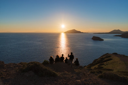 Silhouette of people is watching sunset over the sea and cliffs.