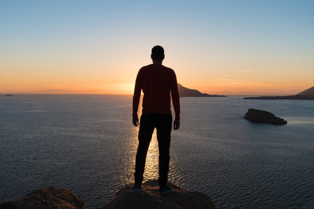 Silhouette of man is watching sunset over the sea and cliffs.の写真素材