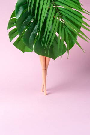 Tropical palm tree leaves with doll legs on pink background. Creative minimal summer concept.の写真素材