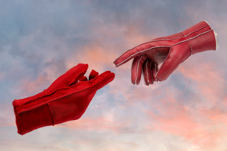 Two leather gloves touching with fingers on sky background. Minimal art concept.の写真素材