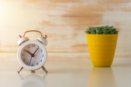 White alarm clock with cactus in pot on wooden desk.の写真素材