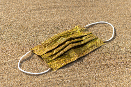 Gold face mask with shiny glitter on sand background. Minimal outbreak. Pandemic concept.の写真素材