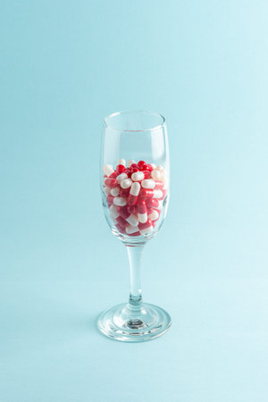 Creative view of glass with red pills on blue background. Minimal concept.