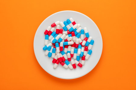 Colorful pills on white plate on orange background. Minimal concept.の写真素材