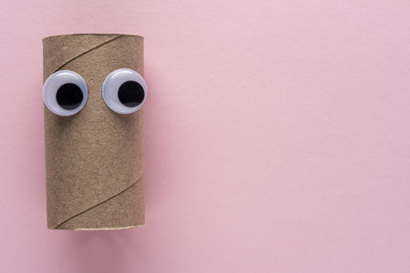 Completed toilet paper roll with googly eyes on pink background.の写真素材